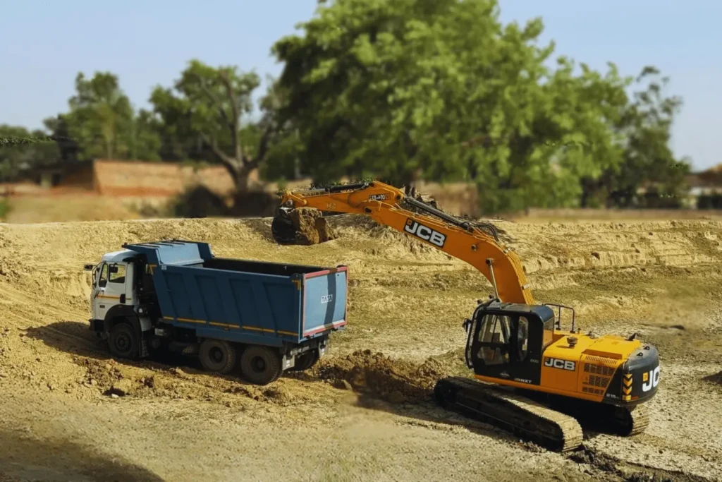 JCB excavator loading soil into a Tata dump truck at a construction site by Trisuka