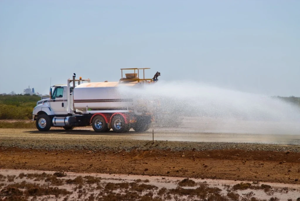 Water tanker spraying water on dusty road at construction site for dust control